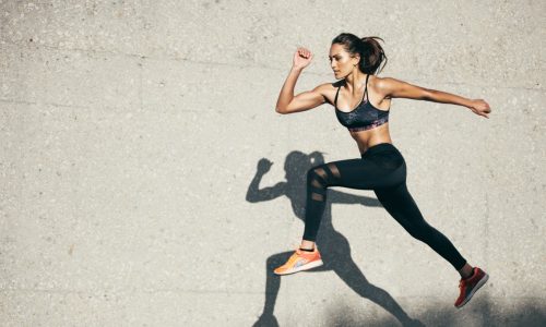 Young,Woman,With,Fit,Body,Jumping,And,Running,Against,Grey